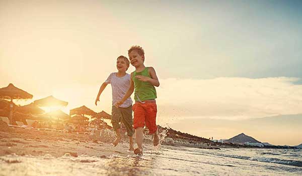 two boys running on a beach in sunshine